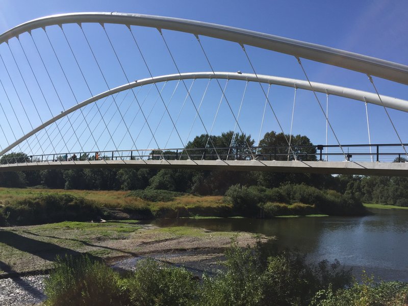 View through the arched steel cables showing pedestrians crossing the bridge deck above the river