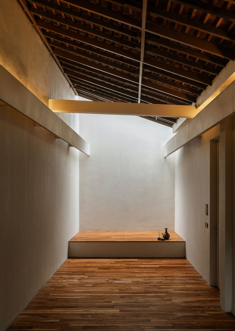 Timber hallway with exposed rafter ceiling and white plaster walls leading to an elevated seating platform