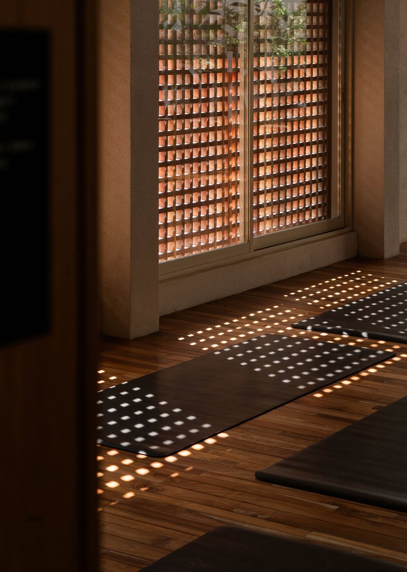 Perforated brick screen window casting dappled sunlight patterns across herringbone timber flooring