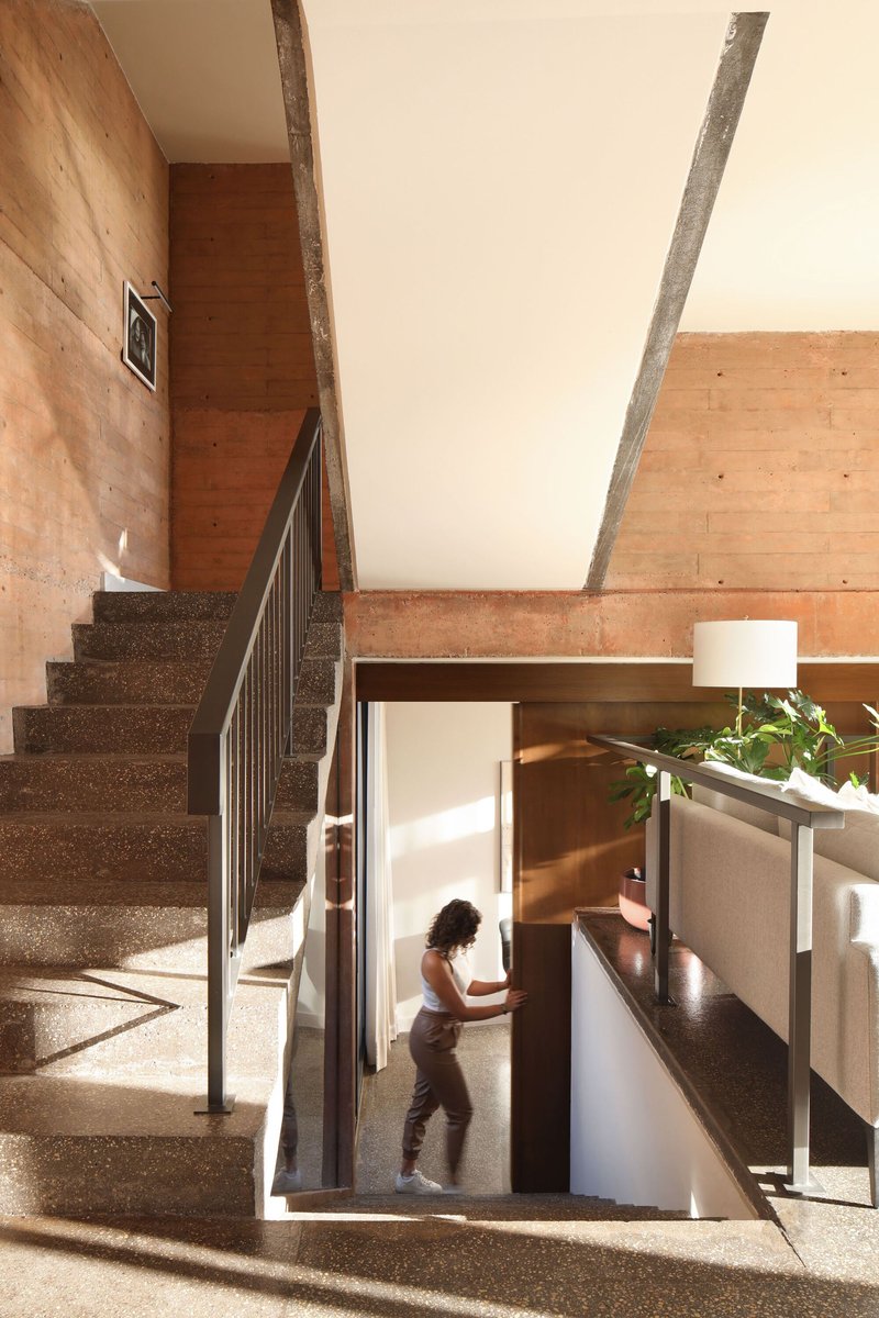 Interior stairwell with exposed concrete beams and figure descending through sunlit opening