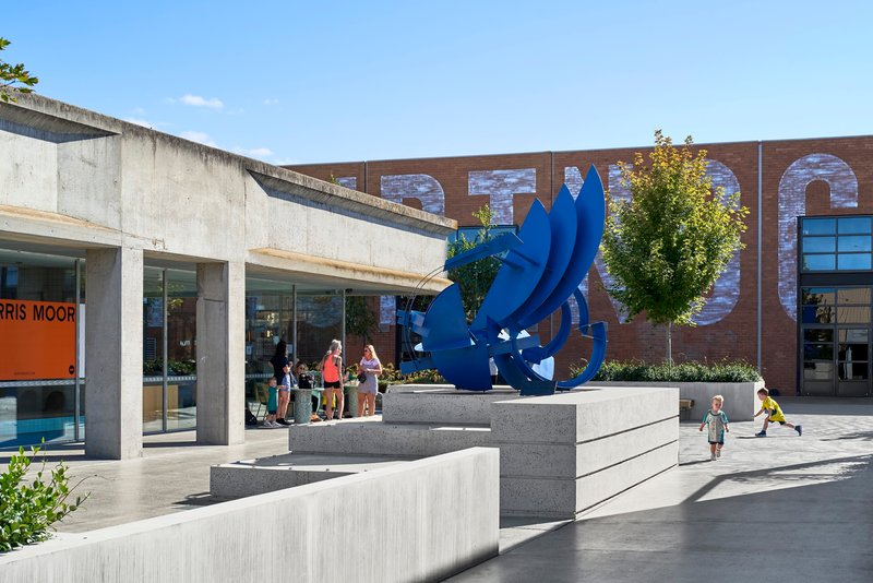 Public courtyard with blue sculpture on concrete plinth steps and brick building facade with oversized lettering
