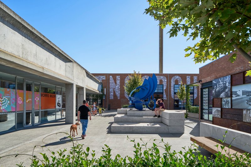 Public plaza with blue sculpture on concrete steps and tree canopy overhead