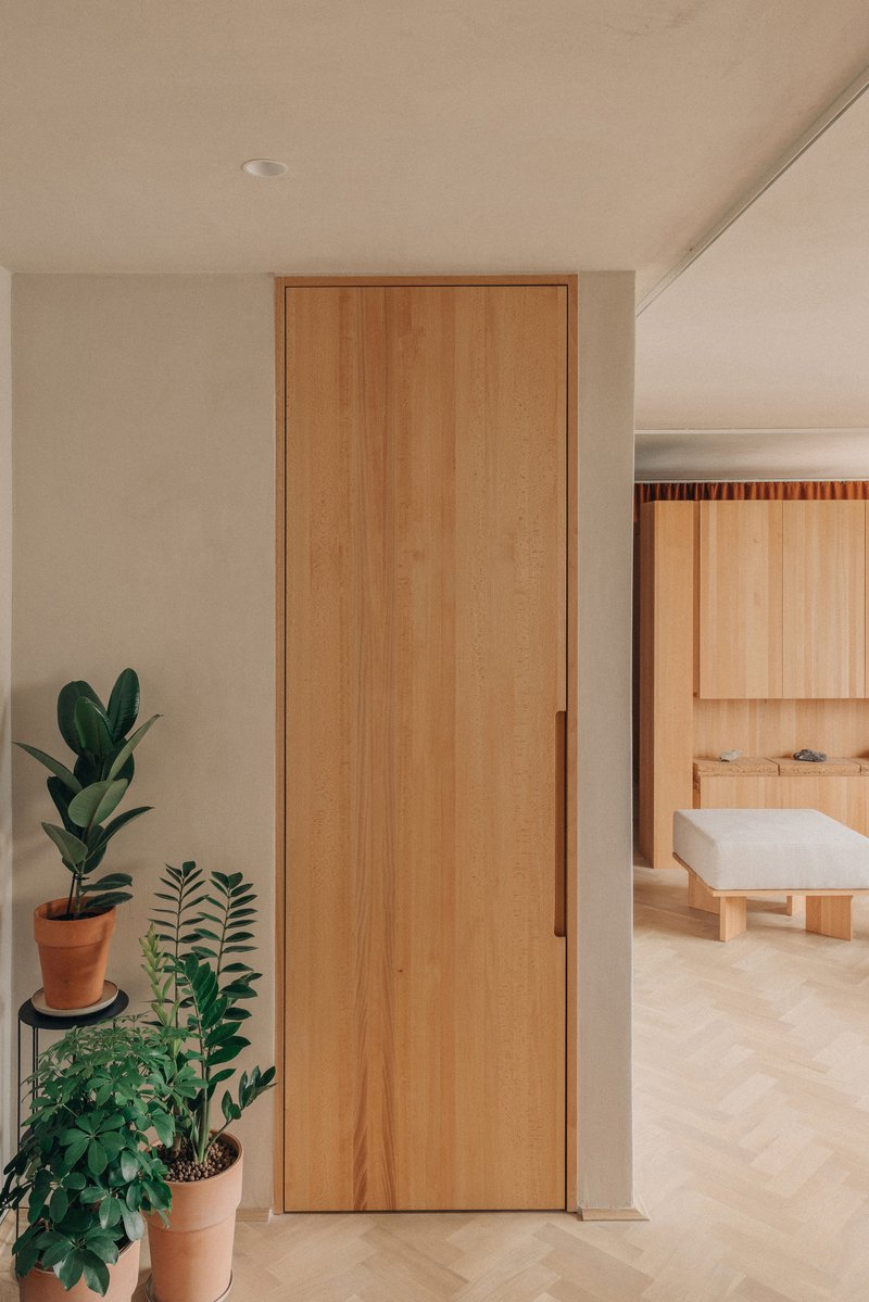 Timber door between white walls with potted plants and view into bathroom with freestanding tub