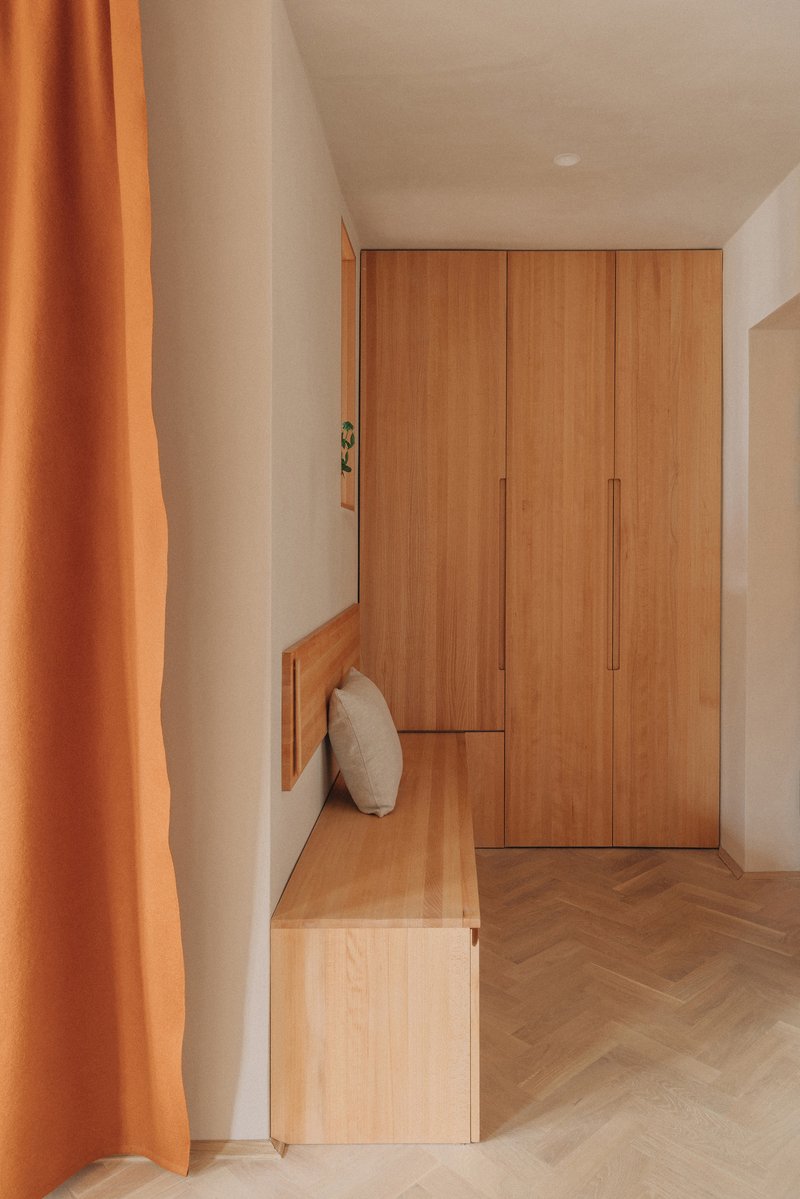 Entryway with timber wardrobe, integrated bench and herringbone flooring partially screened by orange curtain