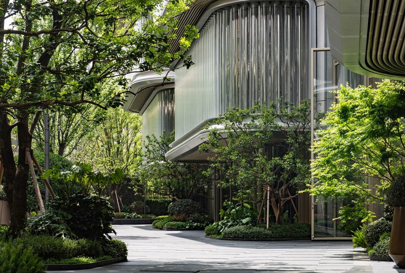 Curved louvered facade nestled among mature trees with ground-level planted beds