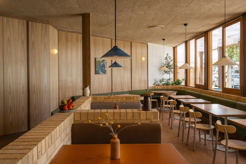 Interior dining area with cream tile banquettes, timber-lined walls, and pendant lights beneath a raw concrete ceiling