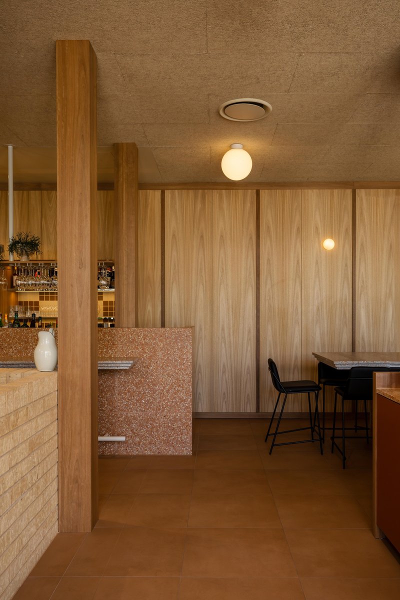 Passage between cream tile counter and timber wall with pink terrazzo detail and globe lights overhead