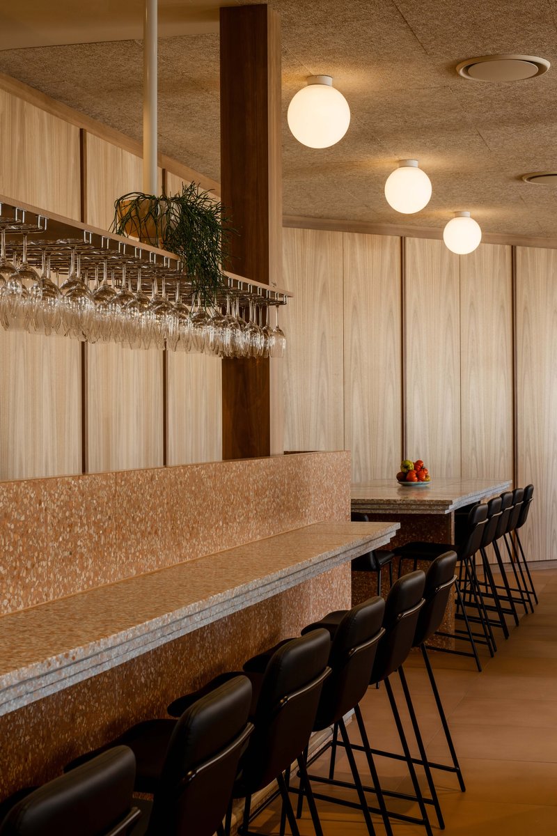 Row of bar stools along terrazzo counter under suspended wine glass storage and globe ceiling lights