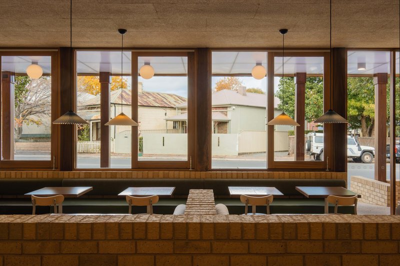 Banquette seating along timber-framed glazing overlooking a residential street in afternoon light