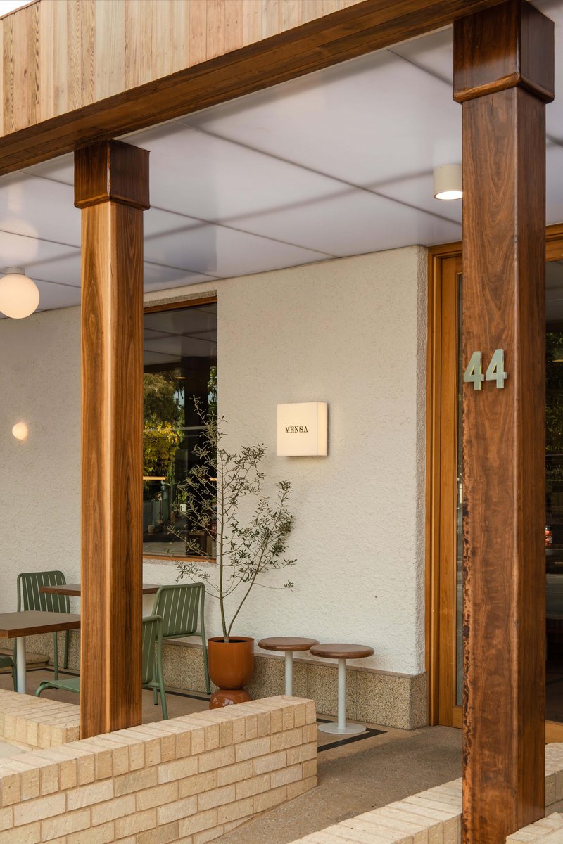 Entry vestibule with timber portal frame, white textured walls, and potted plant beside low brick planter