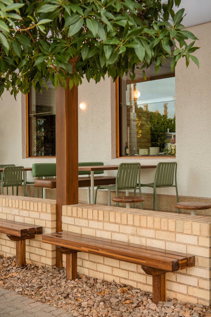 Outdoor terrace at dusk with timber bench against cream brick wall and overhanging tree canopy