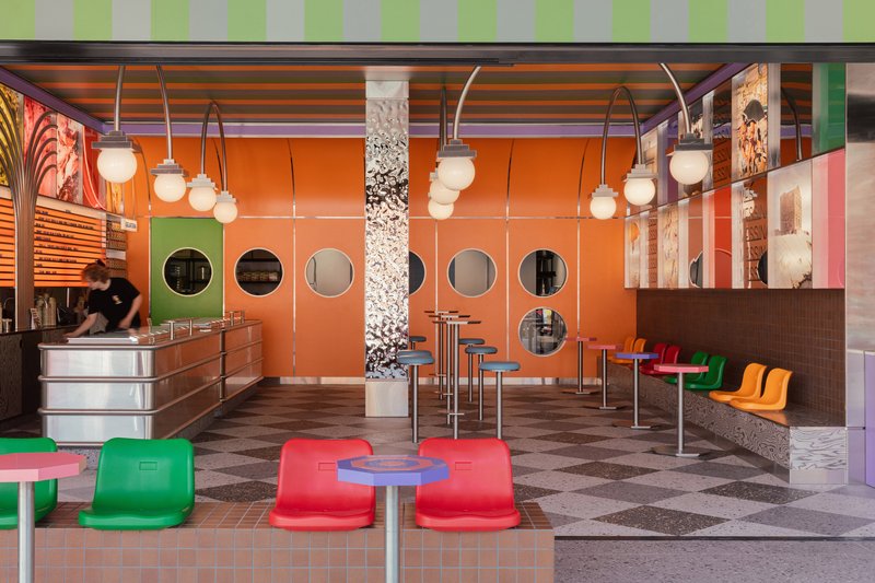 Interior cafe space with orange paneled walls punctured by circular windows and suspended globe pendant lights