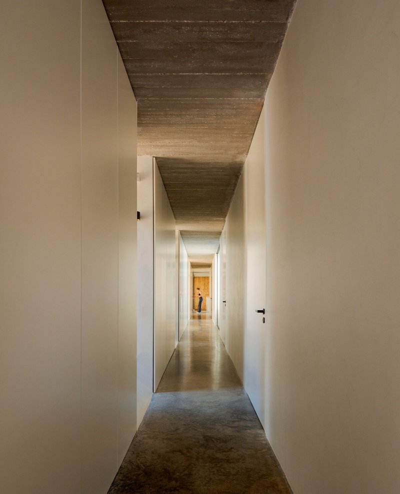 Narrow corridor with board-formed concrete ceiling and white walls leading to a figure at the end