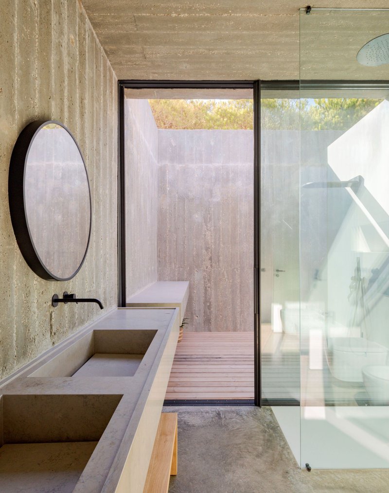 Bathroom with board-formed concrete walls, integrated stone sink and glazed door opening to timber deck