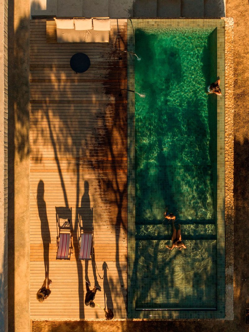 Aerial view of swimming pool and timber deck with four figures casting long shadows at golden hour