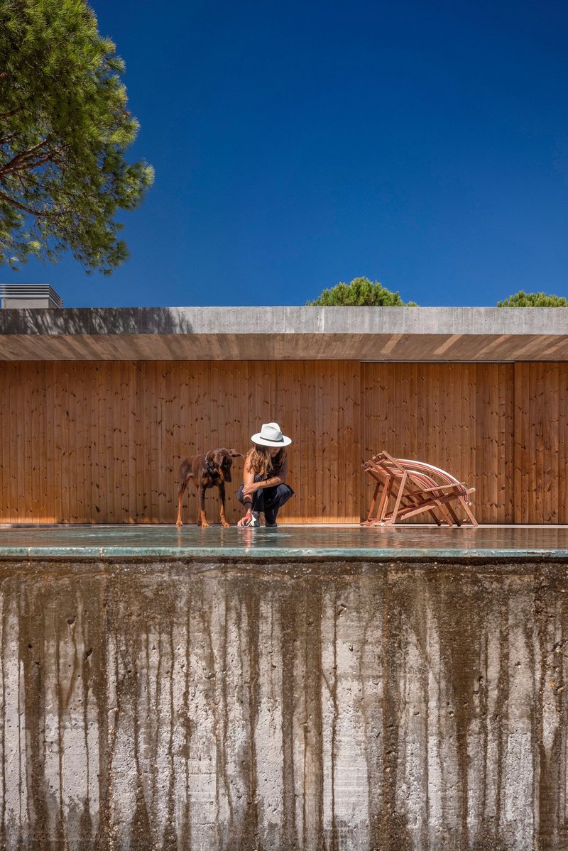 Weathered concrete pool edge with timber wall backdrop where three people gather in midday sun