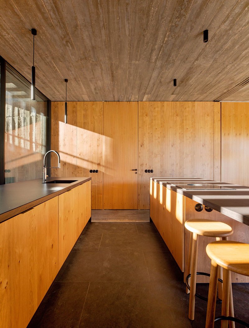Galley kitchen with blonde wood cabinetry and breakfast bar illuminated by afternoon sunlight