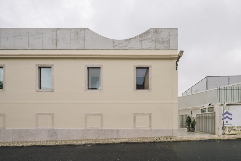 Street view of a cream-coloured facade with recessed panels below square windows and a curved concrete volume above