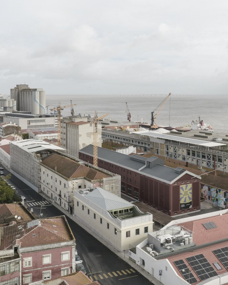 Aerial view of converted warehouse rooftops with port cranes and harbour waters in the background