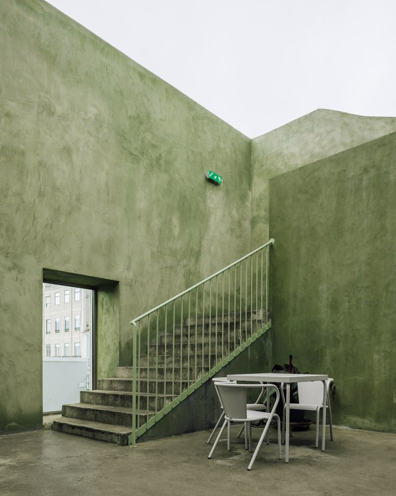 Interior staircase with metal balustrade in a space with pale green polished plaster walls and a table below