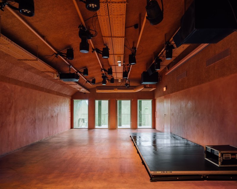 Performance room with terracotta plaster walls, timber ceiling, and retractable stage platform under theatrical lighting