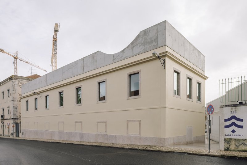 Street corner view showing cream facade with concrete volume above and construction cranes in background