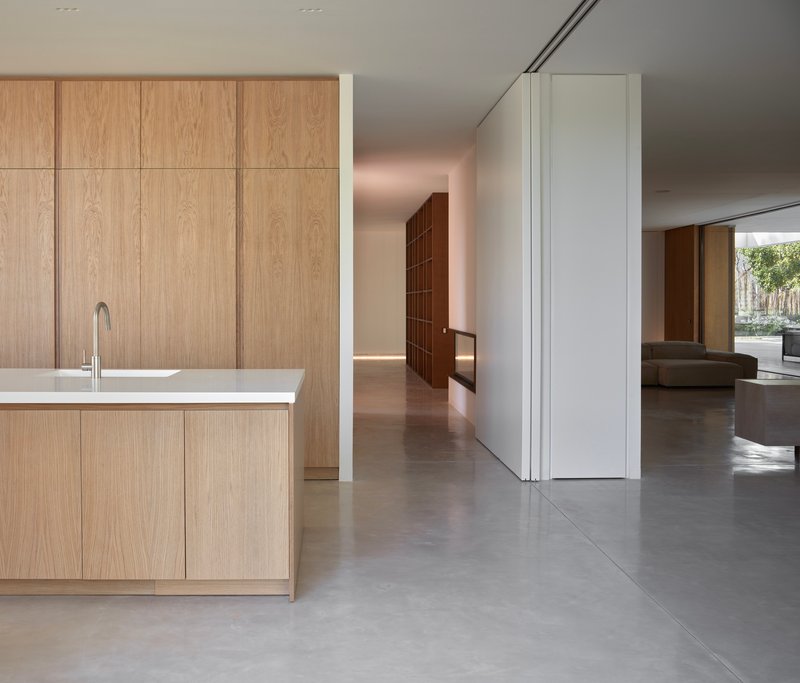 Kitchen island with oak cabinetry on polished concrete floor leading to open living spaces