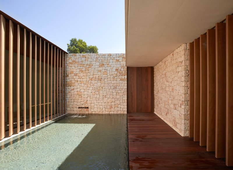 Covered walkway with timber decking alongside the pool edge and stone block walls under midday sun