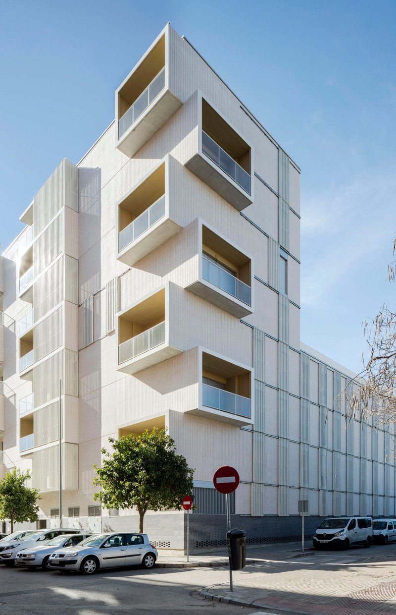 Staggered white facade with projecting balconies and ribbed panel cladding seen from the street