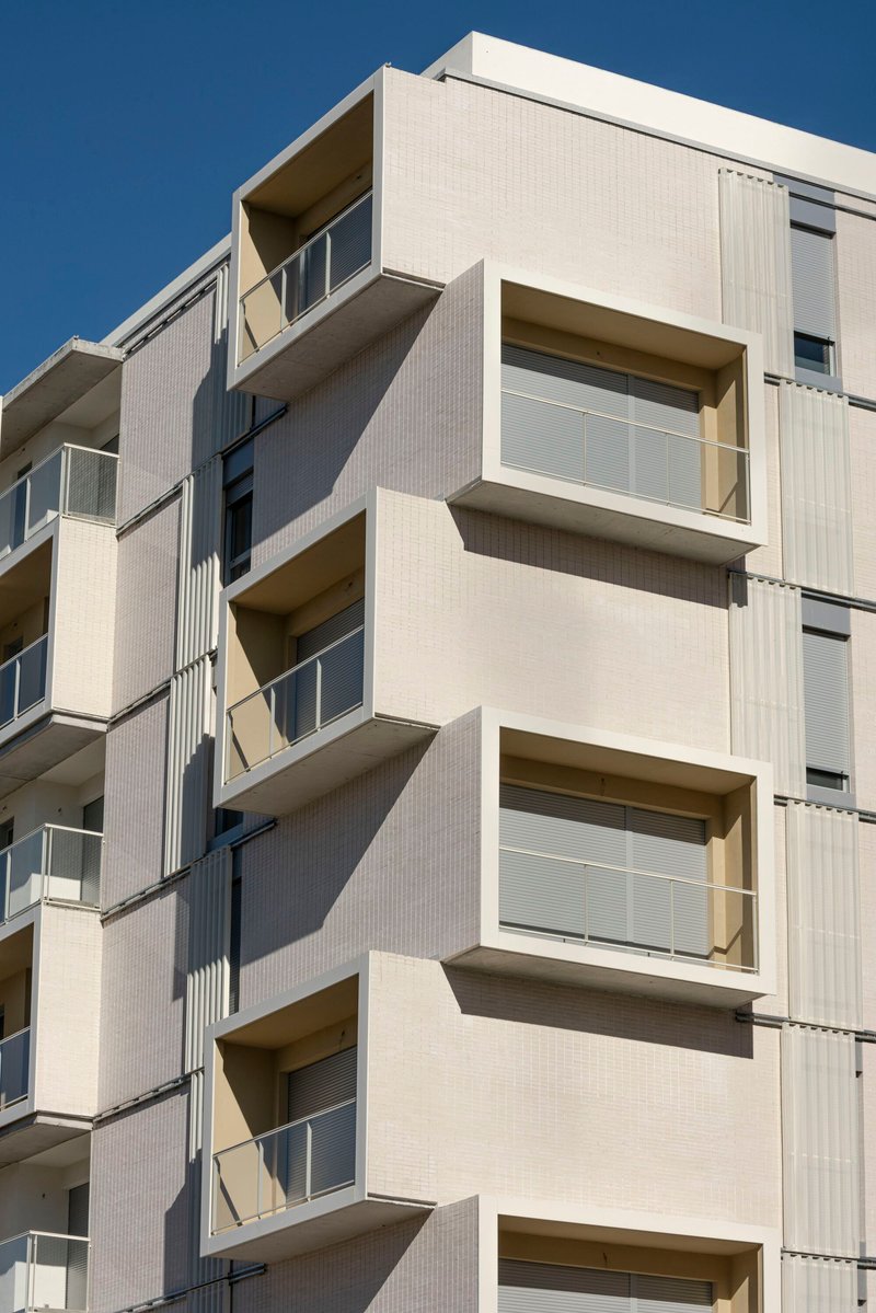Close-up of stacked balconies with glass railings and white ribbed cladding in afternoon sunlight