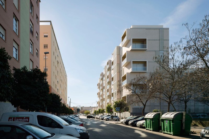 Street view of the stepped facade with recessed balconies, adjacent to parked cars and recycling bins