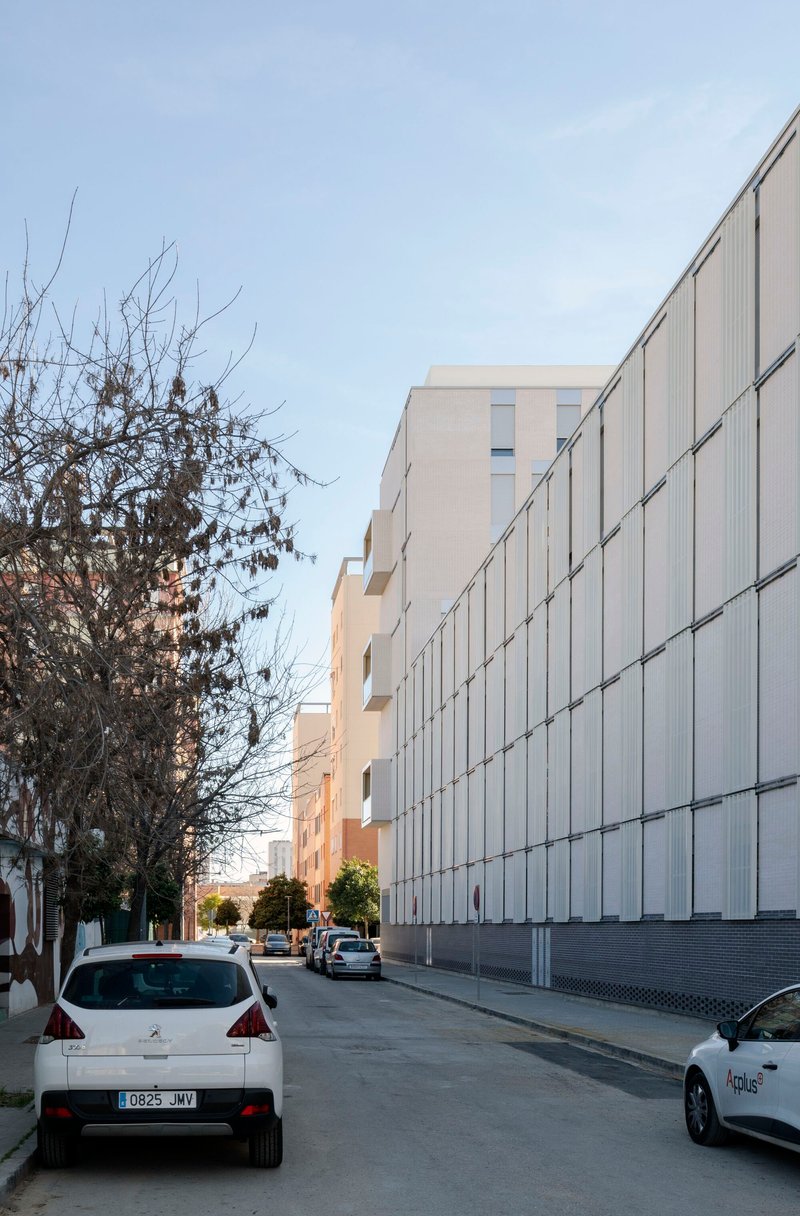 Street perspective of the vertical metal panel facade with bare winter trees and parked vehicles