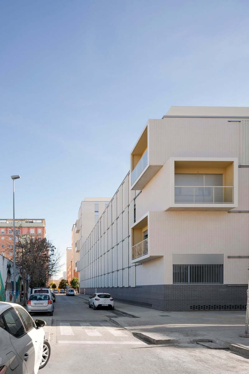 Corner view showing projecting balconies with yellow reveals and the metal panel facade in afternoon light