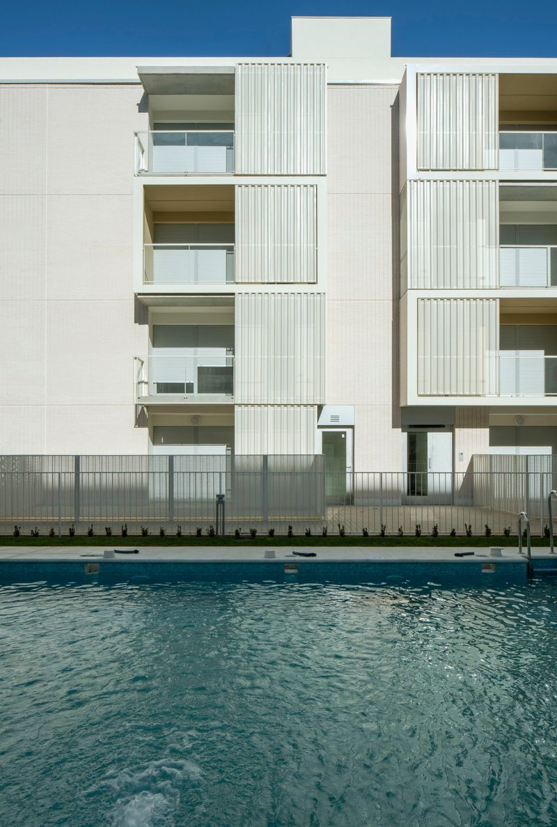 Poolside view of the white facade with recessed balconies and vertical louvers in clear daylight