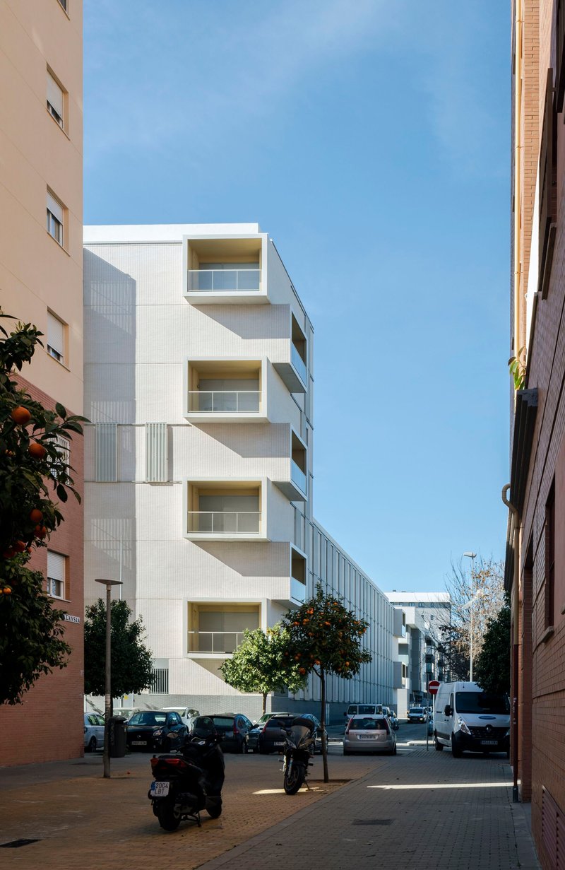 Street view through neighboring buildings showing the white facade with cantilevered balconies and street trees