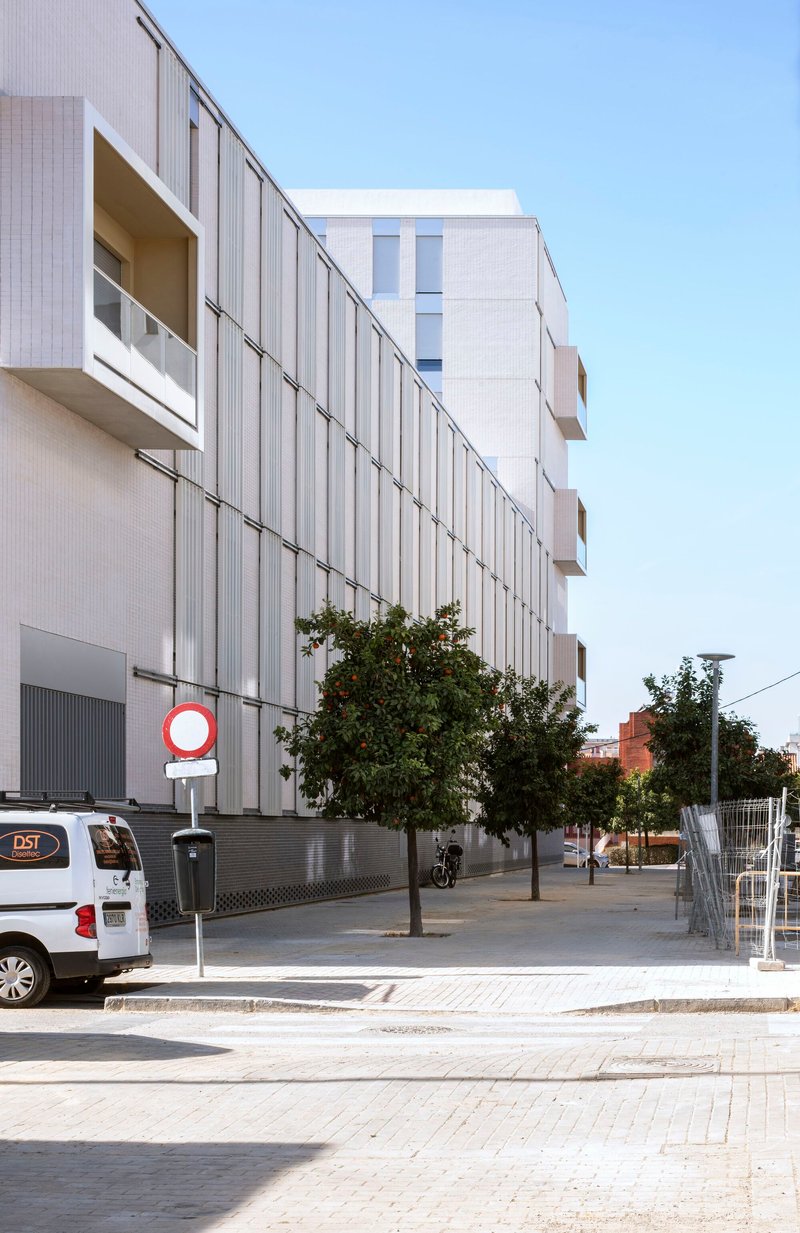 Long facade with vertical metal screening and street trees along a pedestrian sidewalk at dusk