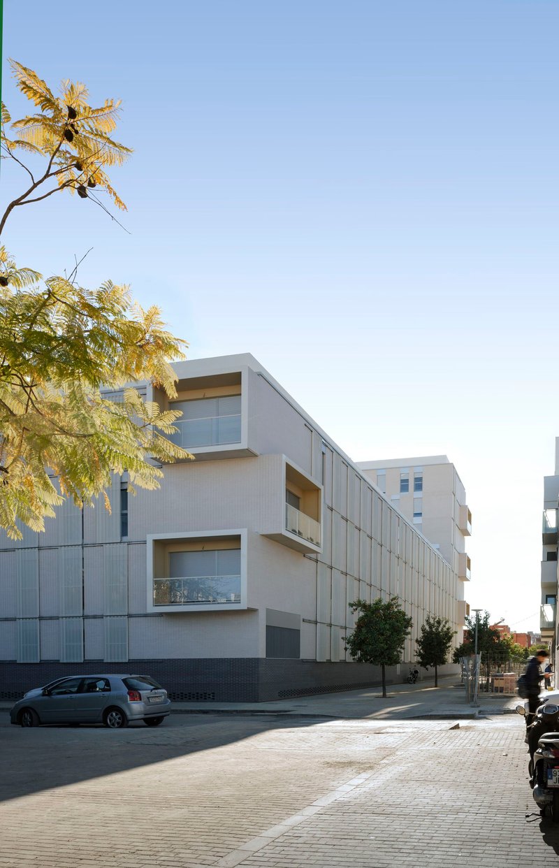 Street view of the white paneled facade with projecting balconies and a tree in the foreground