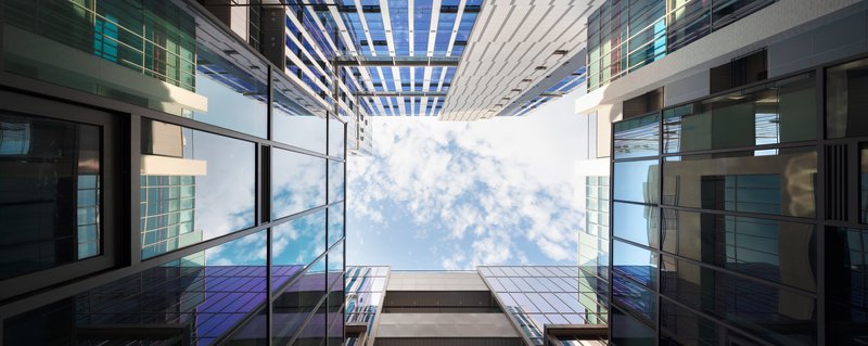 Looking up through the central atrium with glazed walls and a slatted pergola against blue sky and clouds