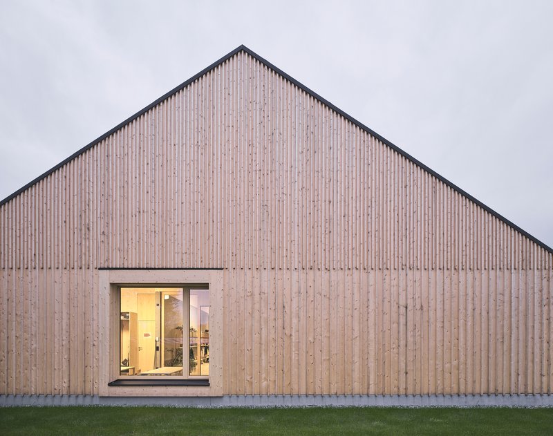 Vertical timber slat gable facade with single punched window opening at twilight