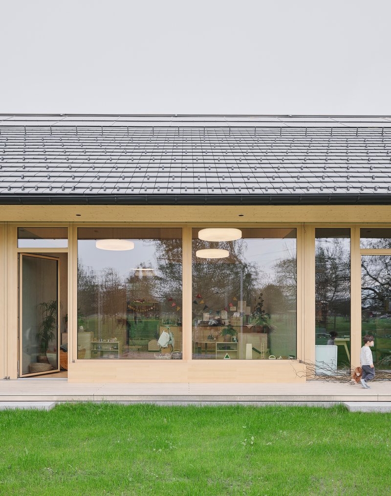 Glazed facade with timber frames beneath deep eave overhang and grey tile roof with child walking