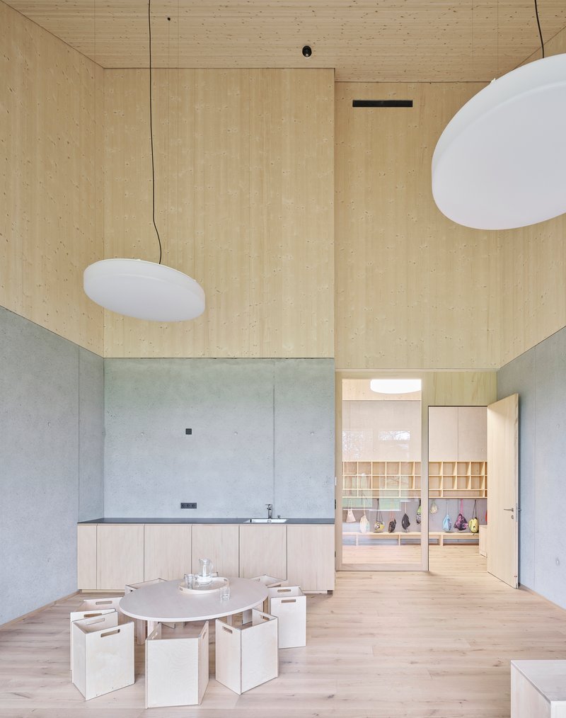 Double-height interior with plywood walls and ceiling above a concrete base and low seating around a table