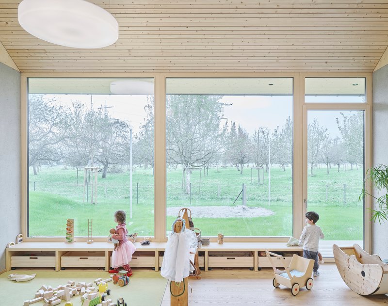 Children playing in a room with floor-to-ceiling windows overlooking the orchard on a misty morning