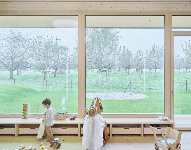 Two children at the window bench with wooden toys looking out to the fenced pasture and trees