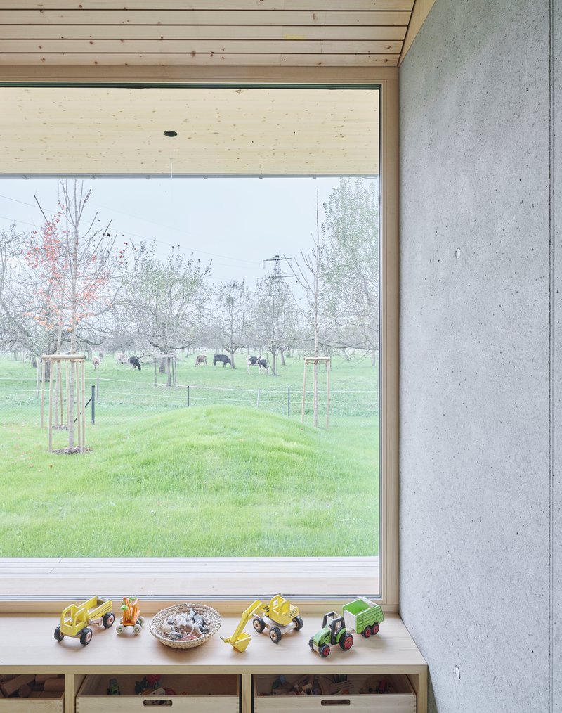 Corner window detail with toy tractors on the sill and cattle grazing beyond the young orchard