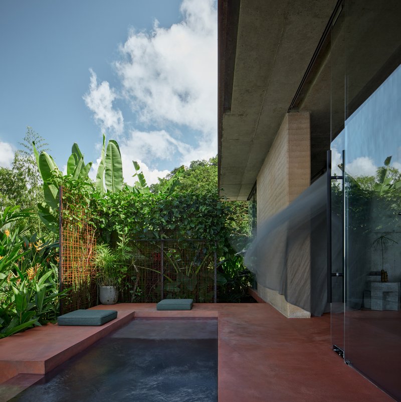 Red-tinted terrace with plunge pool bordered by banana plants and tropical foliage under bright sun