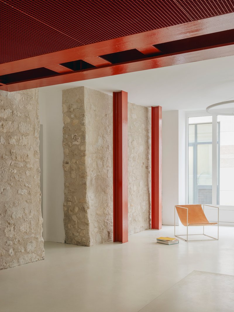 Interior with retained stone walls framed by red steel columns beneath a perforated metal ceiling