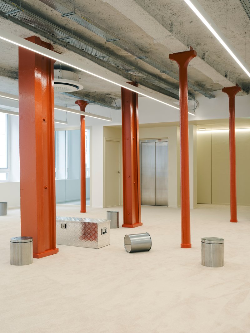 Open floor plate with orange flared steel columns supporting exposed concrete ceiling with linear lights