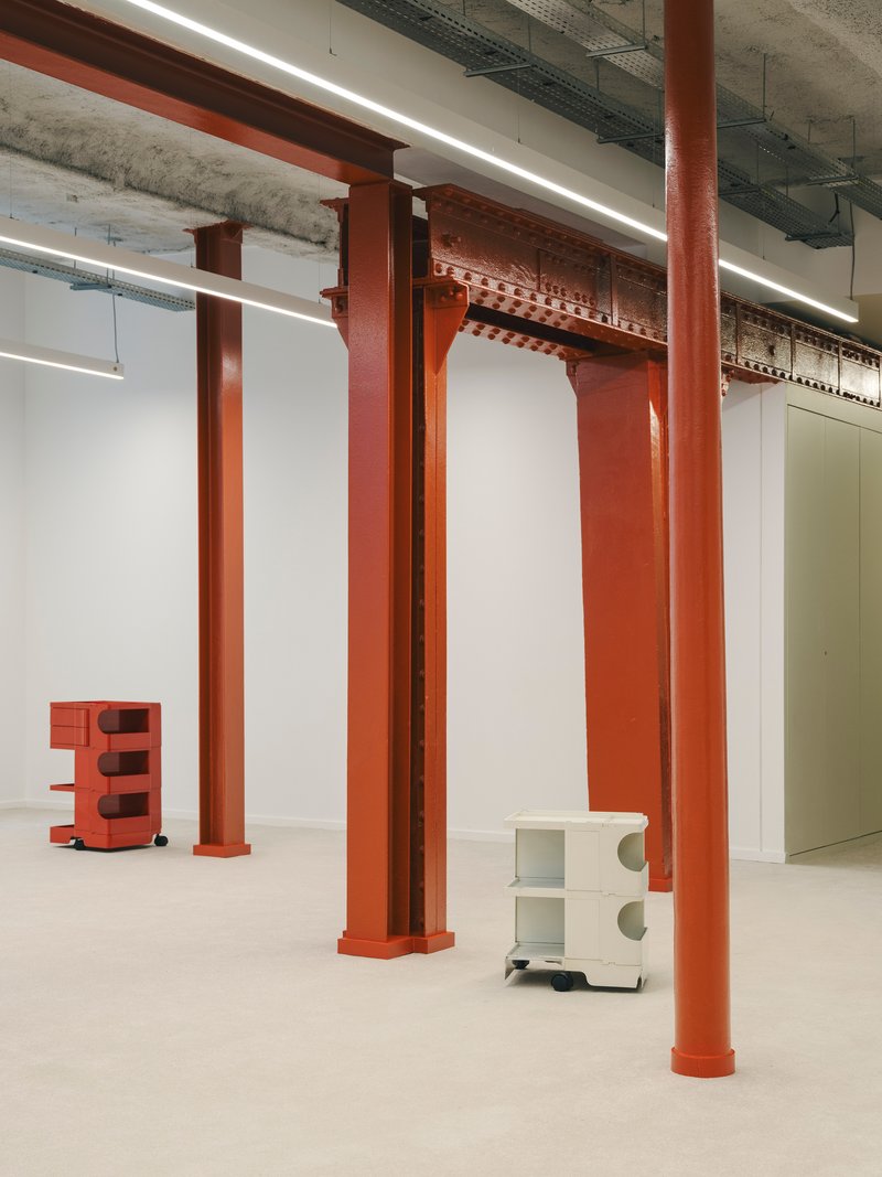 Close view of orange steel columns with decorative capitals beneath exposed concrete structure and services