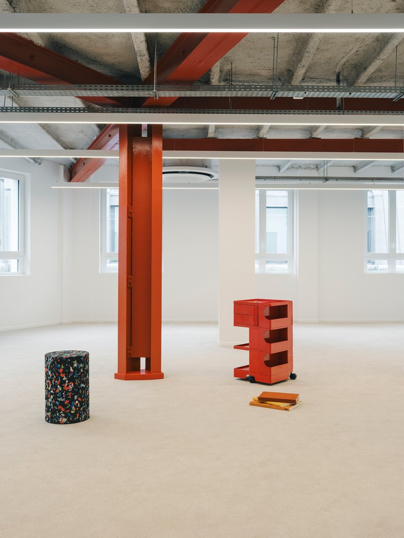 Open floor with orange column, terrazzo cylinder and wheeled storage unit beneath exposed structure