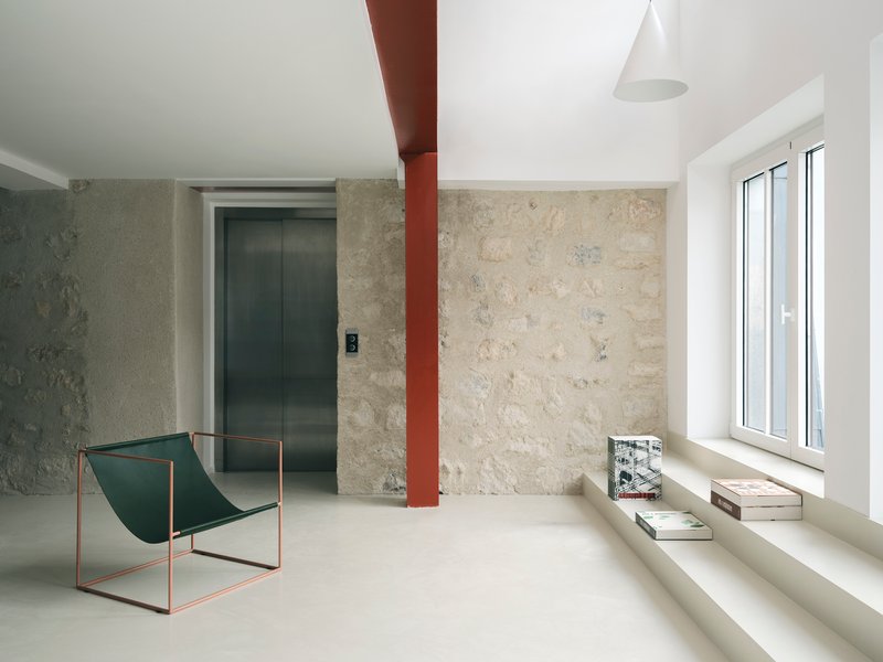 Room with textured limestone walls, a red steel column, and a metal sling chair beside a window